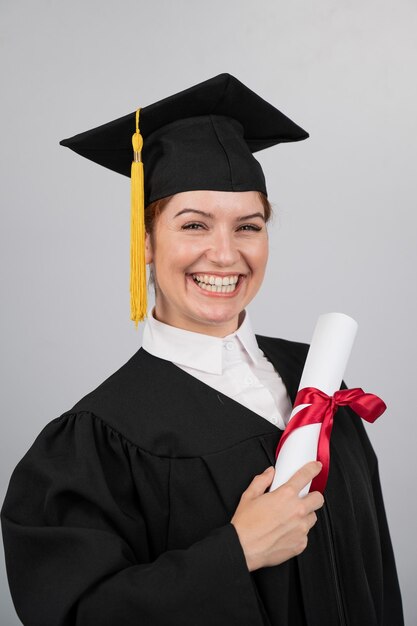 Foto mujer sonriente en vestido de graduación sosteniendo un diploma en una foto vertical de fondo blanco