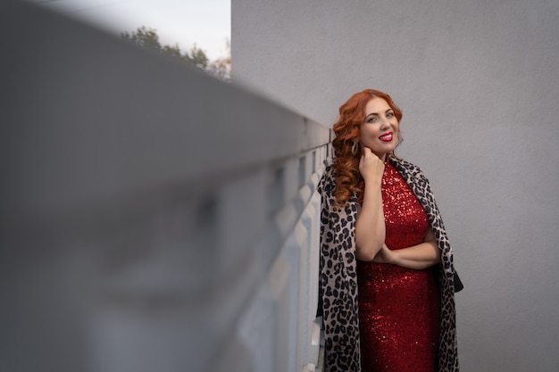 Una mujer sonriente con un vestido de noche rojo se encuentra en el balcón