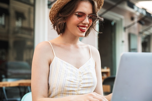 Mujer sonriente en vestido y sombrero de paja con ordenador portátil