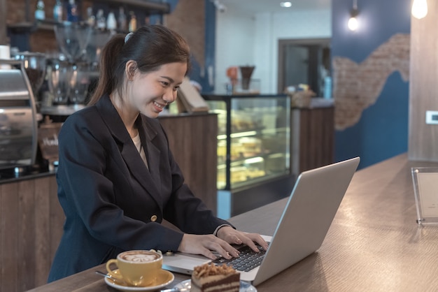 Mujer de sonrisa mirando portátil y papel cuadriculado con energía en cafetería