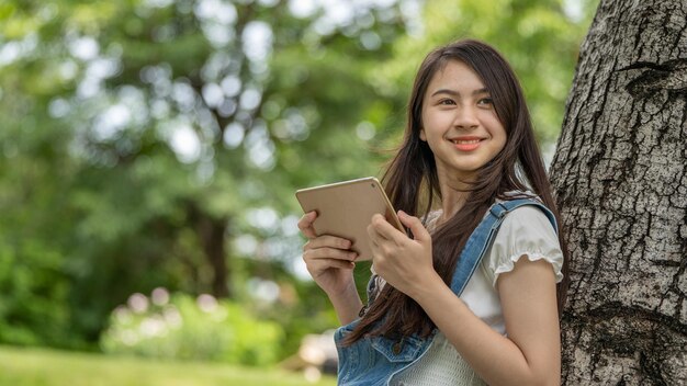 Mujer de sonrisa pensativa en el parque usando tableta digital inteligente Retrato de un joven negocio encantador