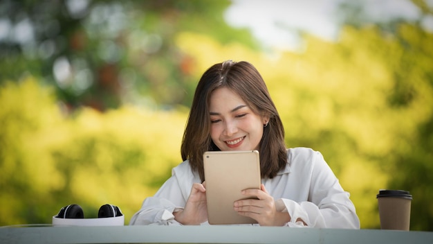 Mujer de sonrisa pensativa en el parque usando tableta digital inteligente Retrato de un joven negocio encantador