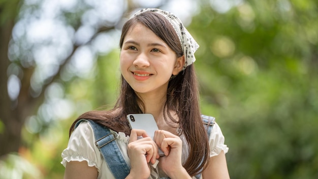 Mujer de sonrisa pensativa en el parque usando un teléfono inteligente Retrato de una joven mujer de negocios encantadora