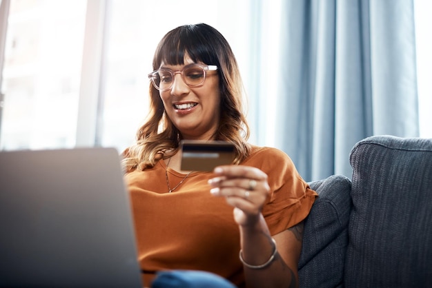 Mujer sonrisa y portátil con tarjeta de débito en el sofá para compras en línea pago y plan de ahorro crédito de la sala de estar y feliz en el sofán en casa para el presupuesto de banca por Internet y la inversión o las finanzas