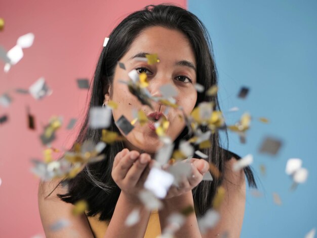 Foto mujer soplando confeti contra un fondo de color