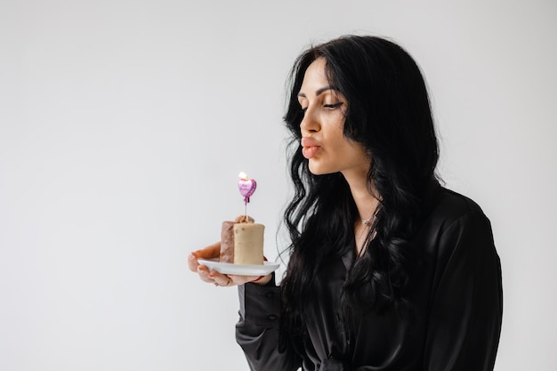 Foto una mujer soplando un pastel de cumpleaños con una vela en forma de corazón.