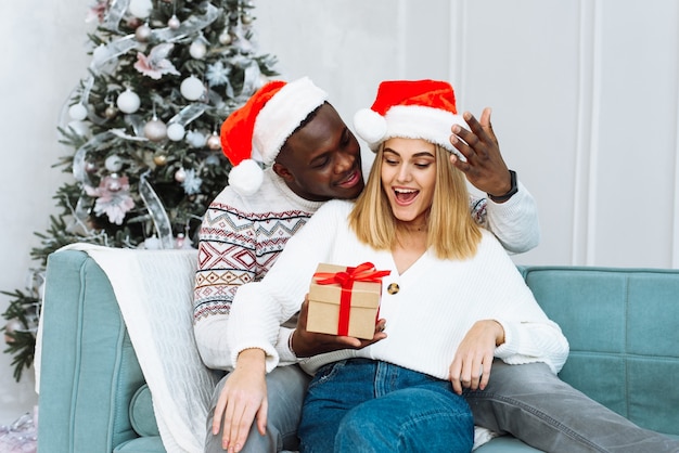 Una mujer se sorprende por el regalo que le dio su marido. Pareja compartiendo regalo de Navidad. Retrato de una pareja encantadora en Navidad