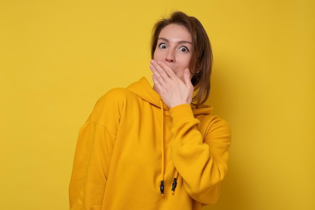 La mujer se sorprende tapándose la boca con la mano, aislada en una pared amarilla.