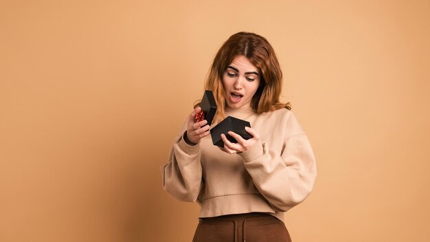 Foto mujer sorprendida abriendo una caja de regalos en un estudio marrón