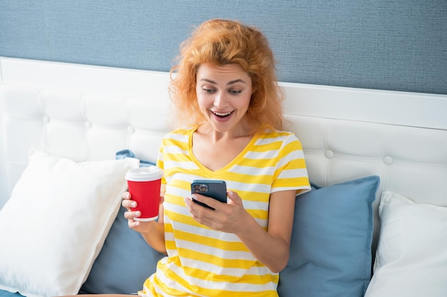 Mujer sorprendida con café blogueando por teléfono mujer blogueando en casa con teléfono blogueando