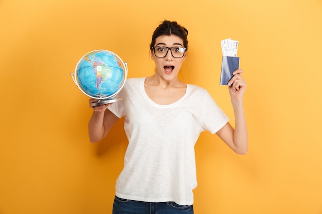 Mujer sorprendida emocionada con gafas sosteniendo globo y pasaporte con boletos.