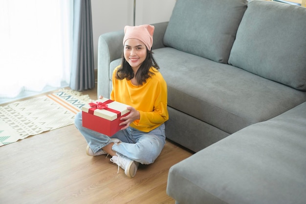 Mujer sorprendida joven que abre una caja de regalo en la sala de estar