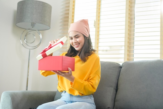 Mujer sorprendida joven que abre una caja de regalo en la sala de estar