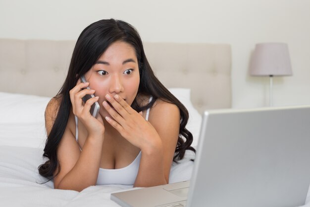 Mujer sorprendida mirando la computadora portátil en el teléfono