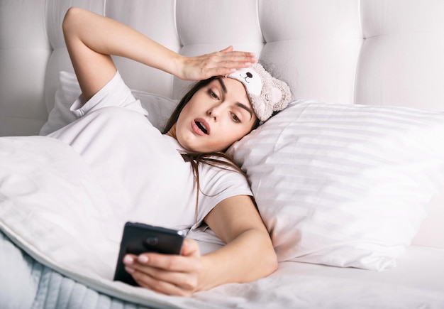 Mujer sorprendida mirando el despertador en el teléfono inteligente y dándose cuenta de que se quedó dormida