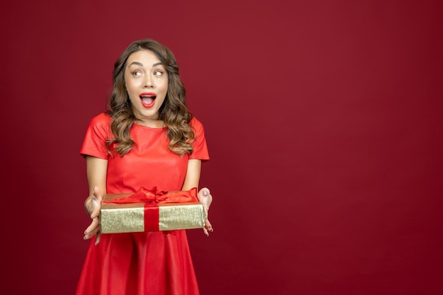 Mujer sorprendida con un regalo en un fondo rojo.