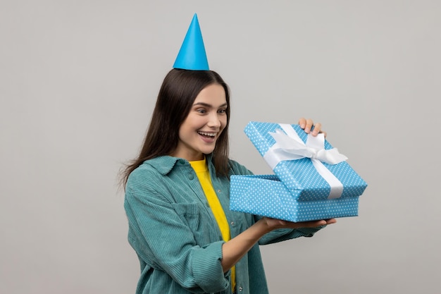 Mujer sorprendida con sombrero de cono de fiesta mirando a la caja de regalo mirando dentro con una sonrisa feliz