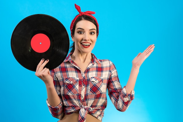 La mujer sorprendida sosteniendo un disco de vinilo sobre el fondo azul.