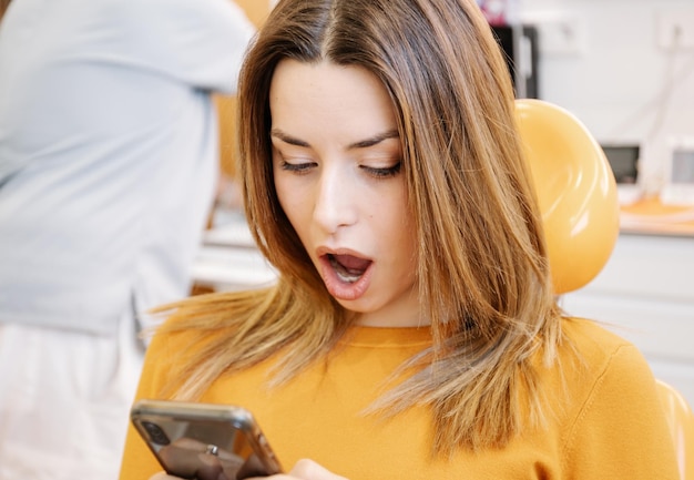 Mujer sorprendida usando un teléfono inteligente en la oficina del dentista