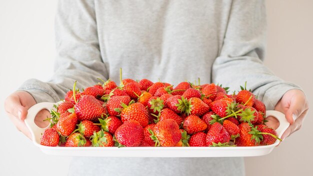 Mujer sostenga la bandeja blanca con fresas maduras rojas