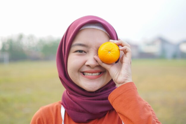 Mujer sostenga fruta naranja y gesto colocado al lado del ojo derecho