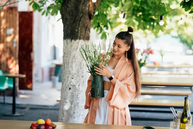 Mujer sostenga un jarrón de flores en el café de la calle