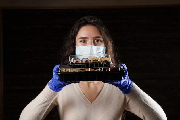 Mujer sosteniendo 2 cajas de sushi en las manos con guantes y mascarilla