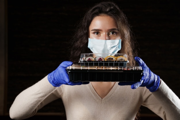 Mujer sosteniendo 2 cajas de sushi en las manos con guantes y mascarilla