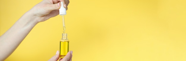 Mujer sosteniendo aceite cosmético en sus manos sobre fondo amarillo closeup