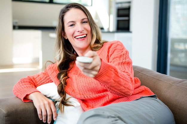 Mujer sosteniendo, acostado en el sofá, un control remoto y sonriendo