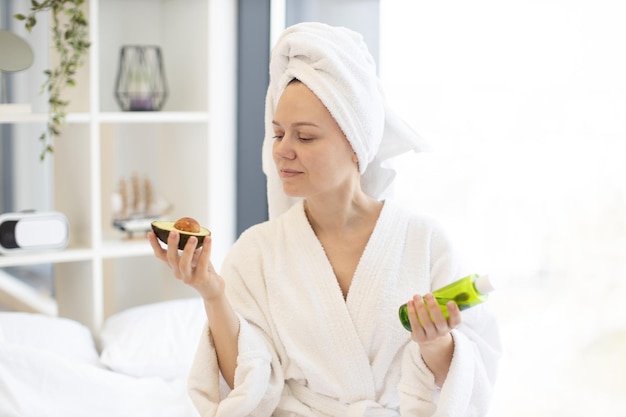 Mujer sosteniendo aguacate y botella de aceite cosmético en el dormitorio