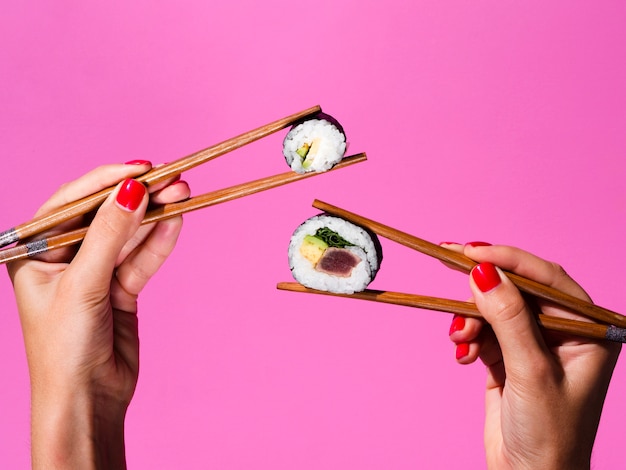 Mujer sosteniendo con ambas manos rollos de sushi en palillos