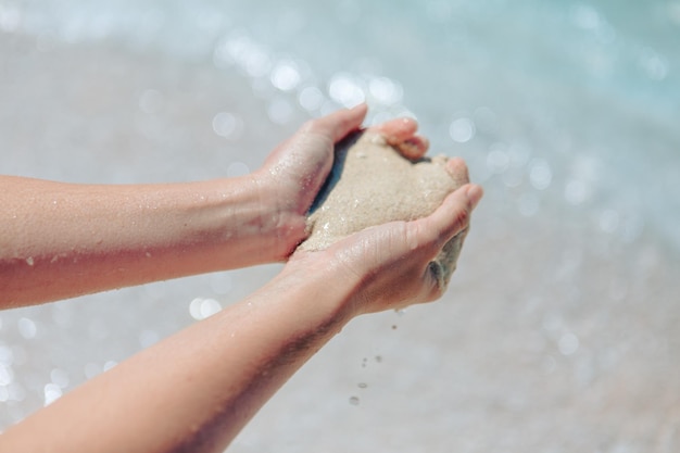 Mujer sosteniendo arena haciendo playa de mar en forma de corazón en el fondo