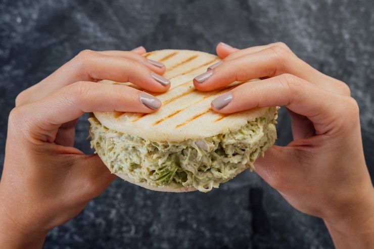 Foto mujer sosteniendo una arepa reina pepeada típica de la cocina venezolana.