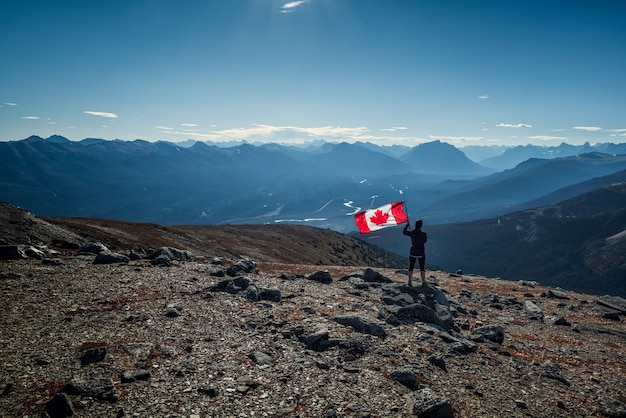 Foto mujer sosteniendo una bandera canadiense en las montañas rocosas canadienses (rockies) en el parque nacional jasper, alberta, canadá.