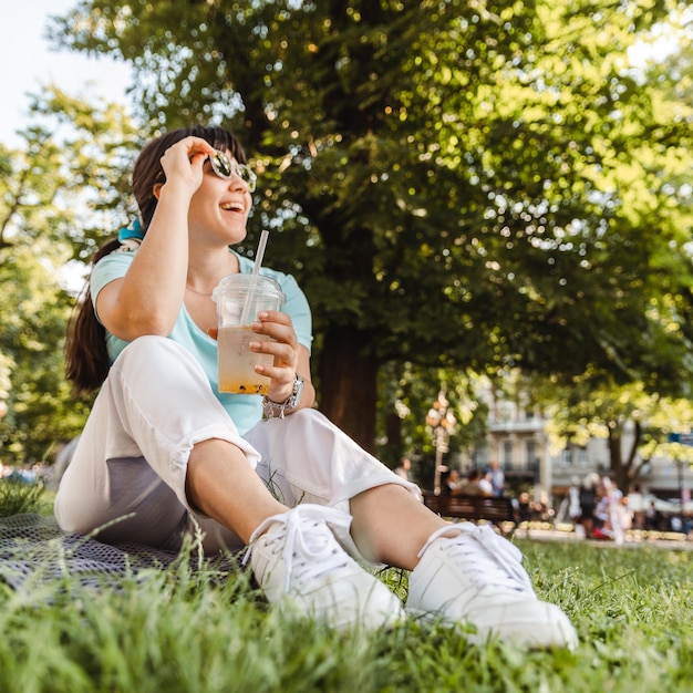 Foto mujer sosteniendo una bebida fría en el parque de la ciudad ángel ancho de fondo borroso