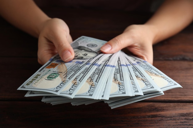 Mujer sosteniendo billetes de dólar en primer plano de la mesa de madera