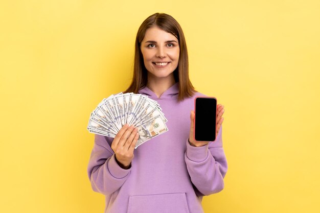 Foto mujer sosteniendo billetes de dólar y teléfono celular con pantalla vacía ganando apuestas en línea