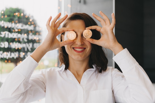 Mujer sosteniendo bitcoin frente a su ojo. Cabeza de mujer de belleza con dinero bitcoin en el ojo. criptomoneda bitcoin.