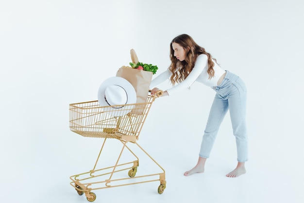 mujer sosteniendo una bolsa de compras llena de comestibles, mango, ensalada, rábano, limón, zanahorias en backgr blanco