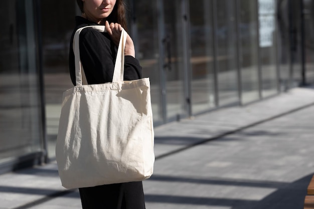 Mujer sosteniendo una bolsa ecológica textil blanca contra el fondo urbano de la ciudad Ecología o concepto de protección del medio ambiente Bolsa ecológica blanca para maqueta