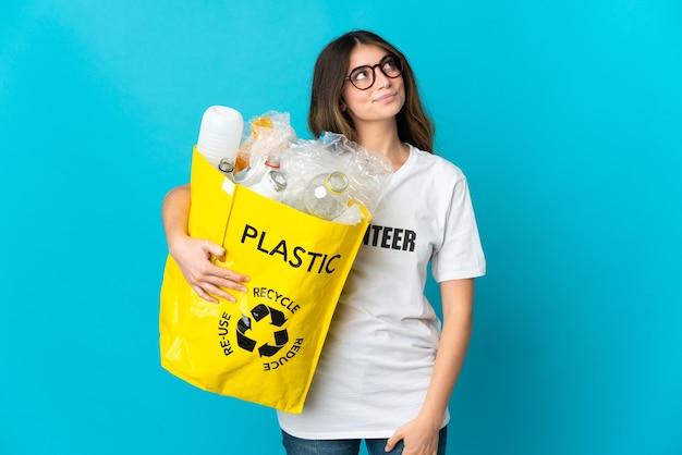 Foto mujer sosteniendo una bolsa llena de botellas para reciclar aislado en azul y mirando hacia arriba