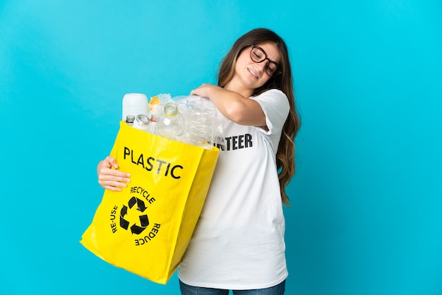 Mujer sosteniendo una bolsa llena de botellas para reciclar aislado en la pared azul que sufre de dolor en el hombro por haber hecho un esfuerzo