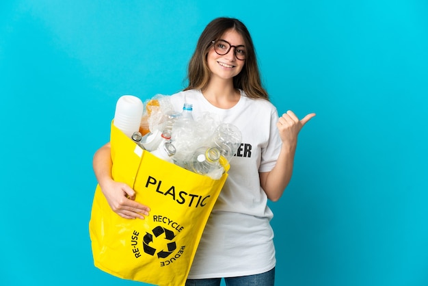 Foto mujer sosteniendo una bolsa llena de botellas para reciclar en azul apuntando hacia el lado para presentar un producto