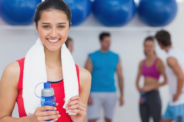 Mujer sosteniendo la botella de agua con clase de fitness en segundo plano