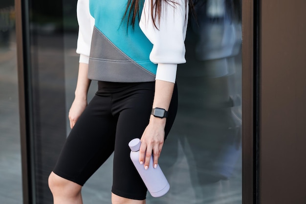 Mujer sosteniendo una botella con agua después del entrenamiento matutino Joven atlética de pie cerca del fondo de la pared oscura después de trotar Concepto de estilo de vida saludable