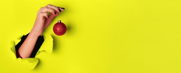 Mujer sosteniendo brillante bola de Navidad roja sobre fondo amarillo