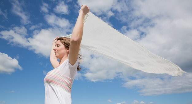 Mujer sosteniendo bufanda contra el cielo azul y las nubes