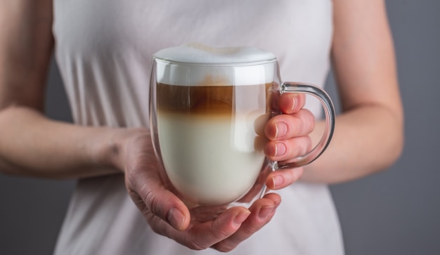 Mujer sosteniendo un café con leche fresco y aromático, vertido en capas en una taza de vidrio doble transparente