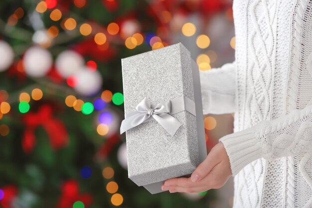 Mujer sosteniendo caja de regalo contra luces de Navidad borrosas